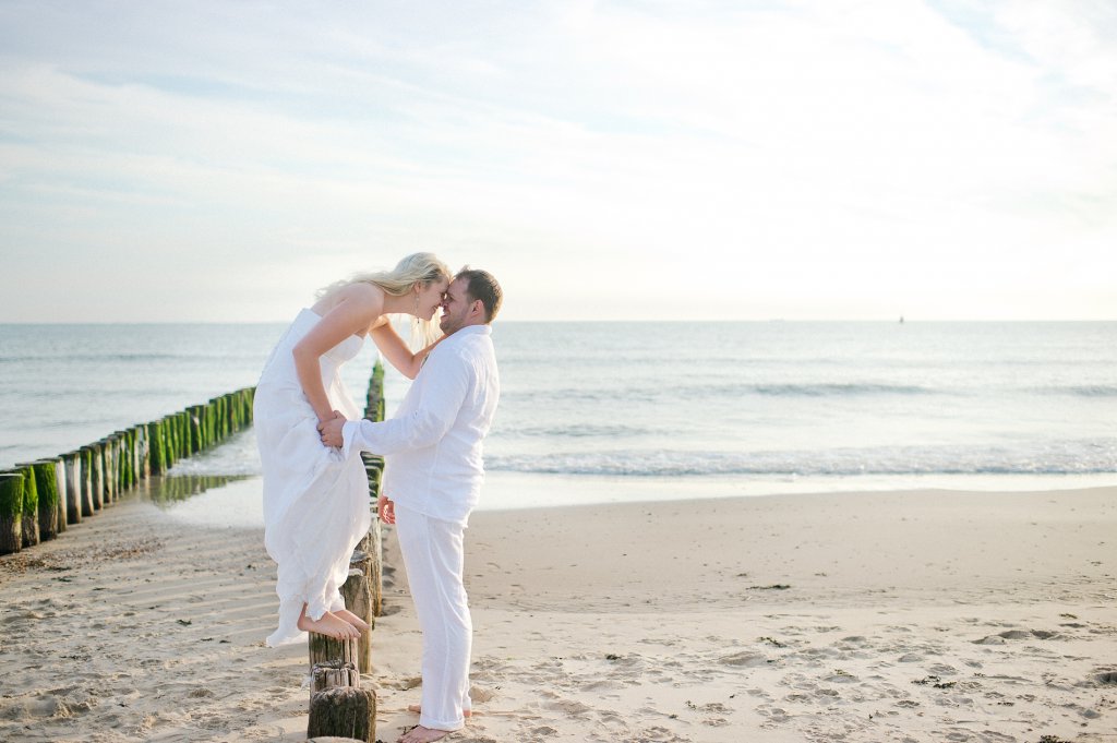 Photo Braut küsst Bräutigam auf Strandpflöcken stehend.